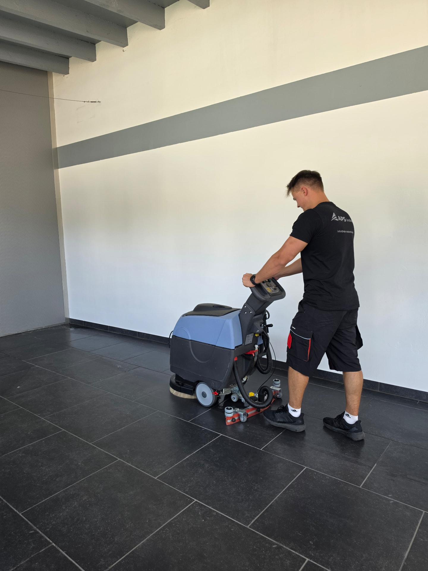 APS Mitarbeiter reinigt Hallenboden mit Scheuersaugmaschine – Hallen- und Gewerbereinigung